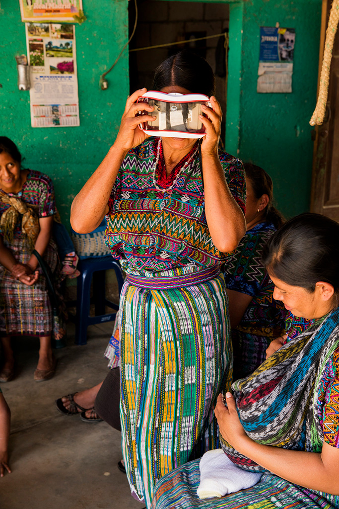 Guatemalan woman in traditional dress holding a virtual reality headset to her face while standing. 